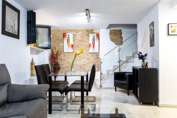 A modern living room with a dining area, a staircase, and a black bookshelf.