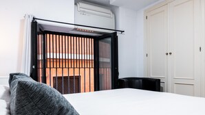 A hotel room with a bed, a window with blinds, a wardrobe, and an air conditioning unit.