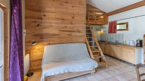 Ein gemütliches Blockhaus mit Holzinnenraum, einer Couch, einer Leiter, einer Küchenzeile und einem Fenster mit rotem Vorhang.