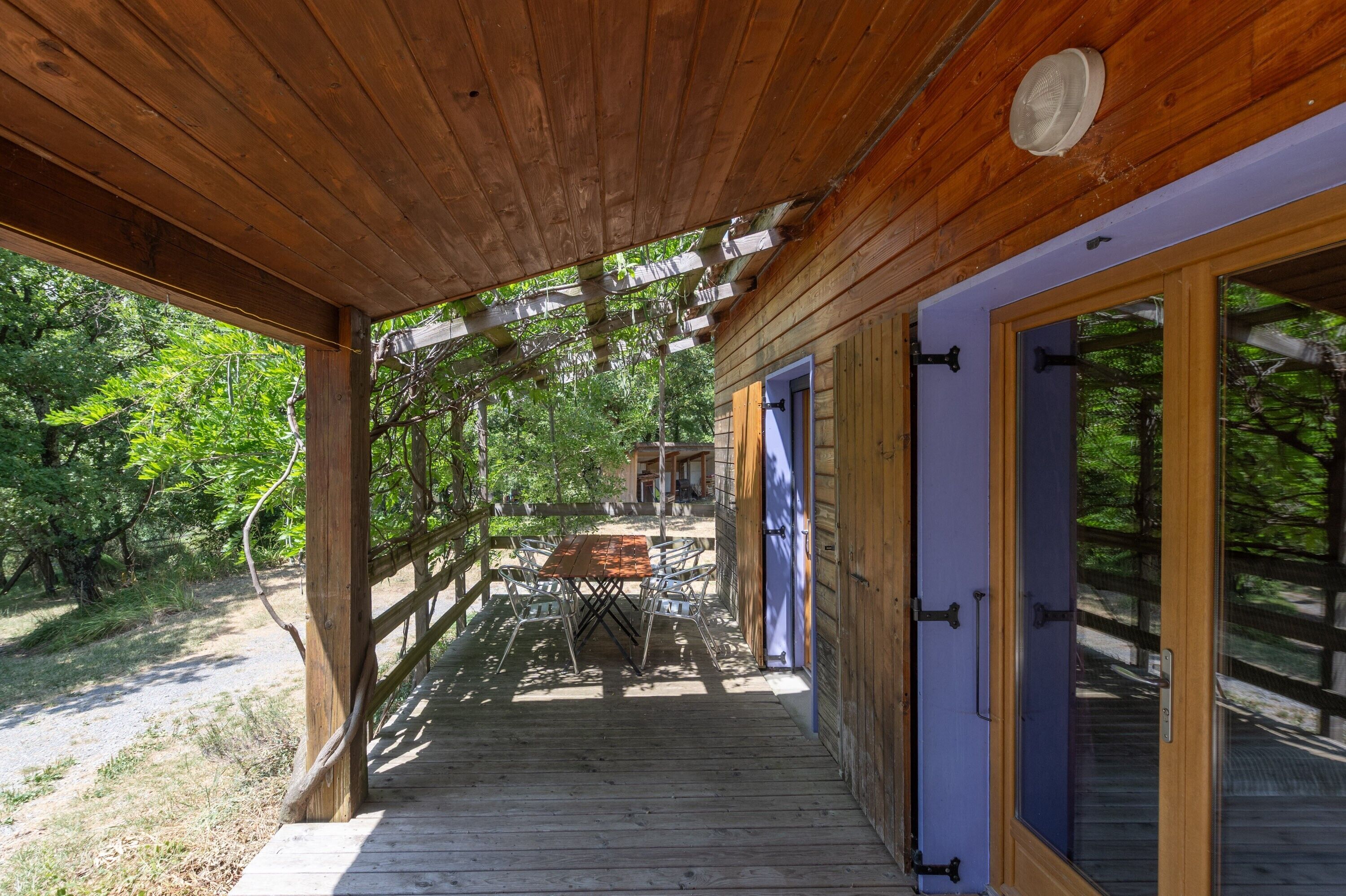 A wooden deck with a table and chairs, a covered area with a ceiling, and a building entrance with glass doors.