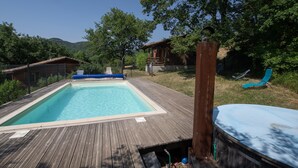 Um deck de madeira com piscina retangular, hidromassagem e uma espreguiçadeira.