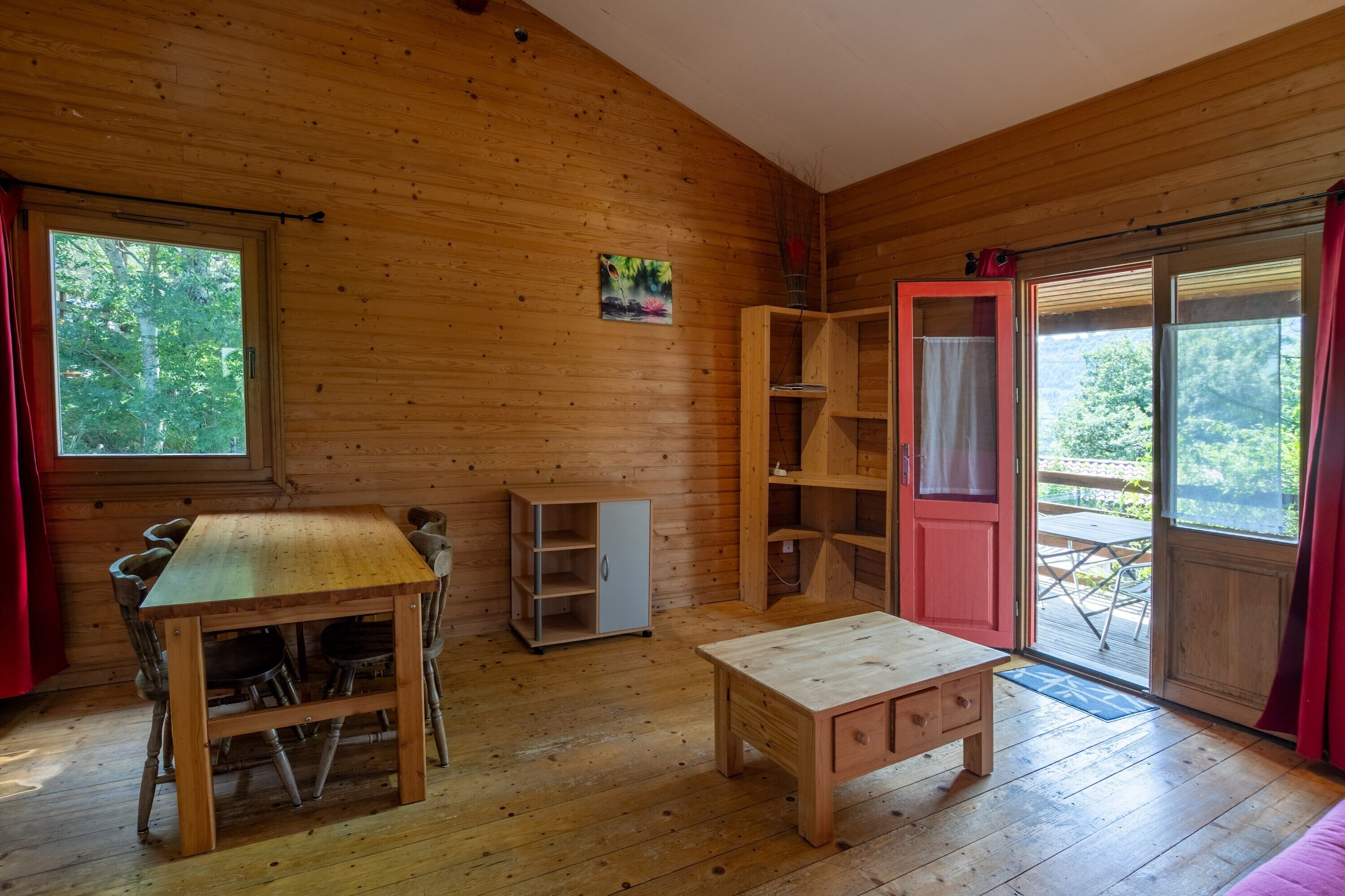 L’intérieur d’un chalet en bois comprend une table à manger, des chaises, un petit meuble et une porte coulissante donnant sur un espace extérieur.