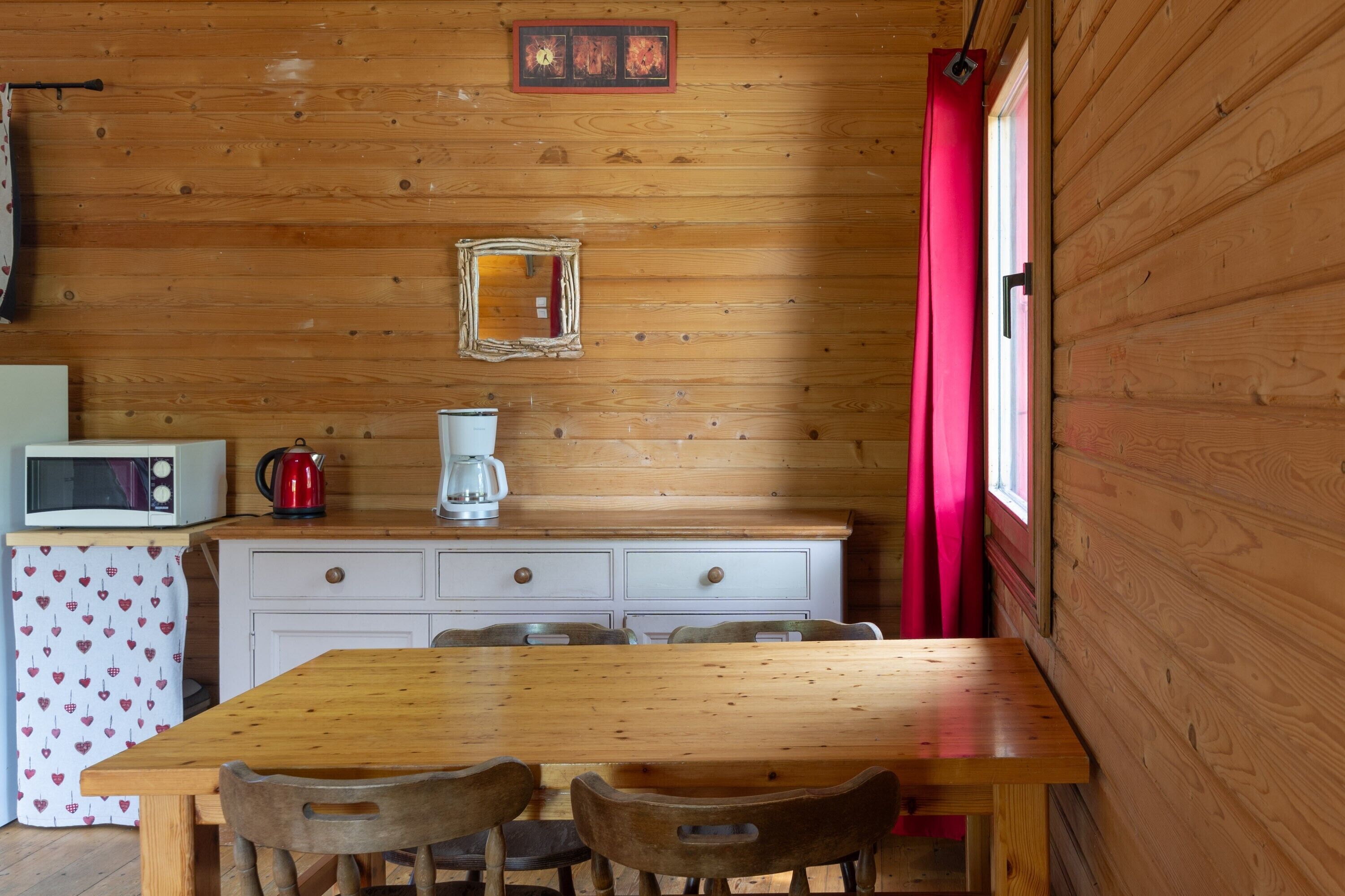 Ein Holzblockhaus-Interieur mit einem Holzesstisch, Stühlen, einer Mikrowelle, einer Kaffeemaschine und einem kleinen Schrank.