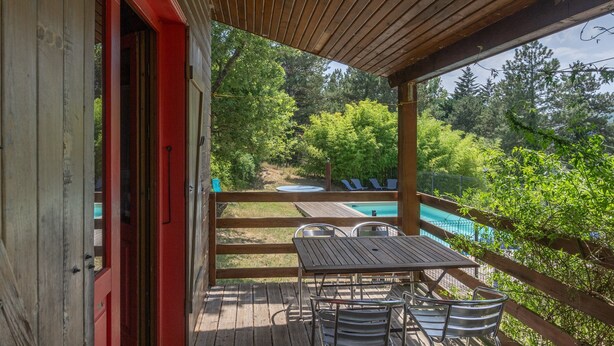 Um deck de madeira com mesa e cadeiras, piscina e vista para árvores.