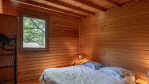 Quarto de cabana de madeira com cama, janela e mesa de cabeceira.