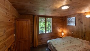 Een houten kamer met een bed, een raam, een nachtkastje en een wandlamp.