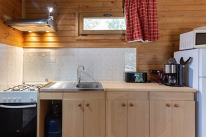 A kitchen with a gas stove, sink, and a window with a red curtain.