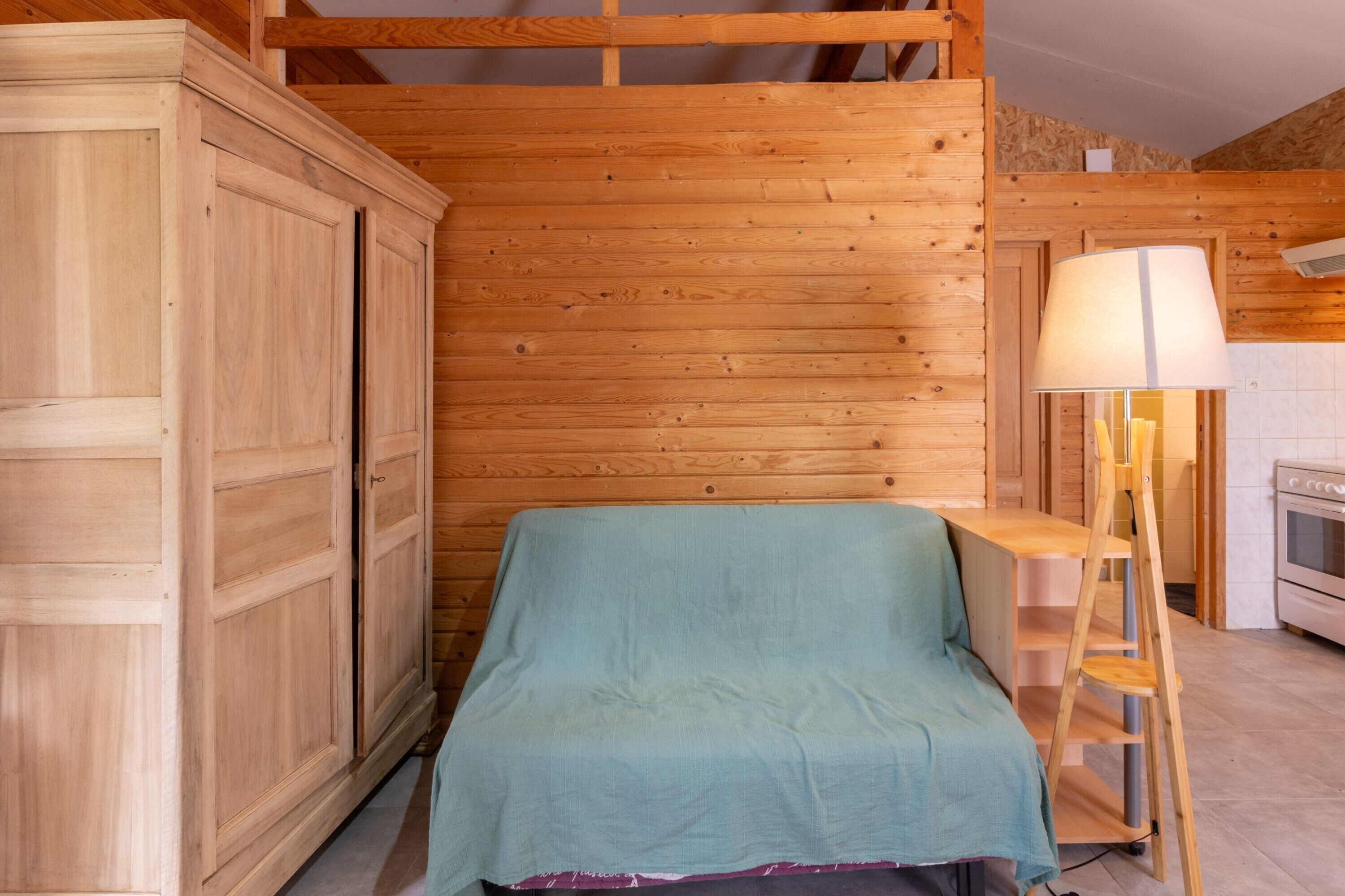 Interior de una cabaña de madera con una cama, un armario de madera, una mesa y una lámpara.