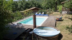 A wooden deck with a hot tub, a pool, and lounge chairs.