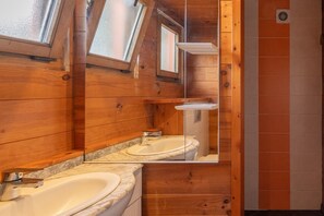 Une salle de bain rustique, aménagée dans une cabane en bois, avec un puits de lumière, un lavabo et un miroir.