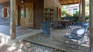 A wooden cabin with a porch, outdoor seating, and a stone building in the background. - Guest House 'Chalet Orange' with Balcony and Wi-Fi (Darbres)