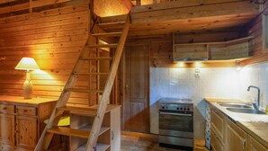 A wooden interior with a staircase, kitchen area including a stove and sink, and a lamp on a wooden table. - Guest House 'Chalet Orange' with Balcony and Wi-Fi (Darbres)