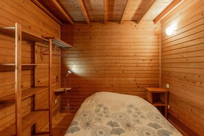 A wooden cabin room with a bed, a desk, and a shelf.