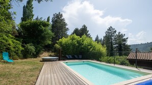 A rectangular swimming pool with a wooden deck, surrounded by greenery and trees. - Guest House 'Chalet Orange' with Balcony and Wi-Fi (Darbres)