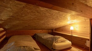 A small attic bedroom with two beds, wooden walls, a slanted ceiling, and a single bedside lamp. - Guest House 'Chalet Orange' with Balcony and Wi-Fi (Darbres)