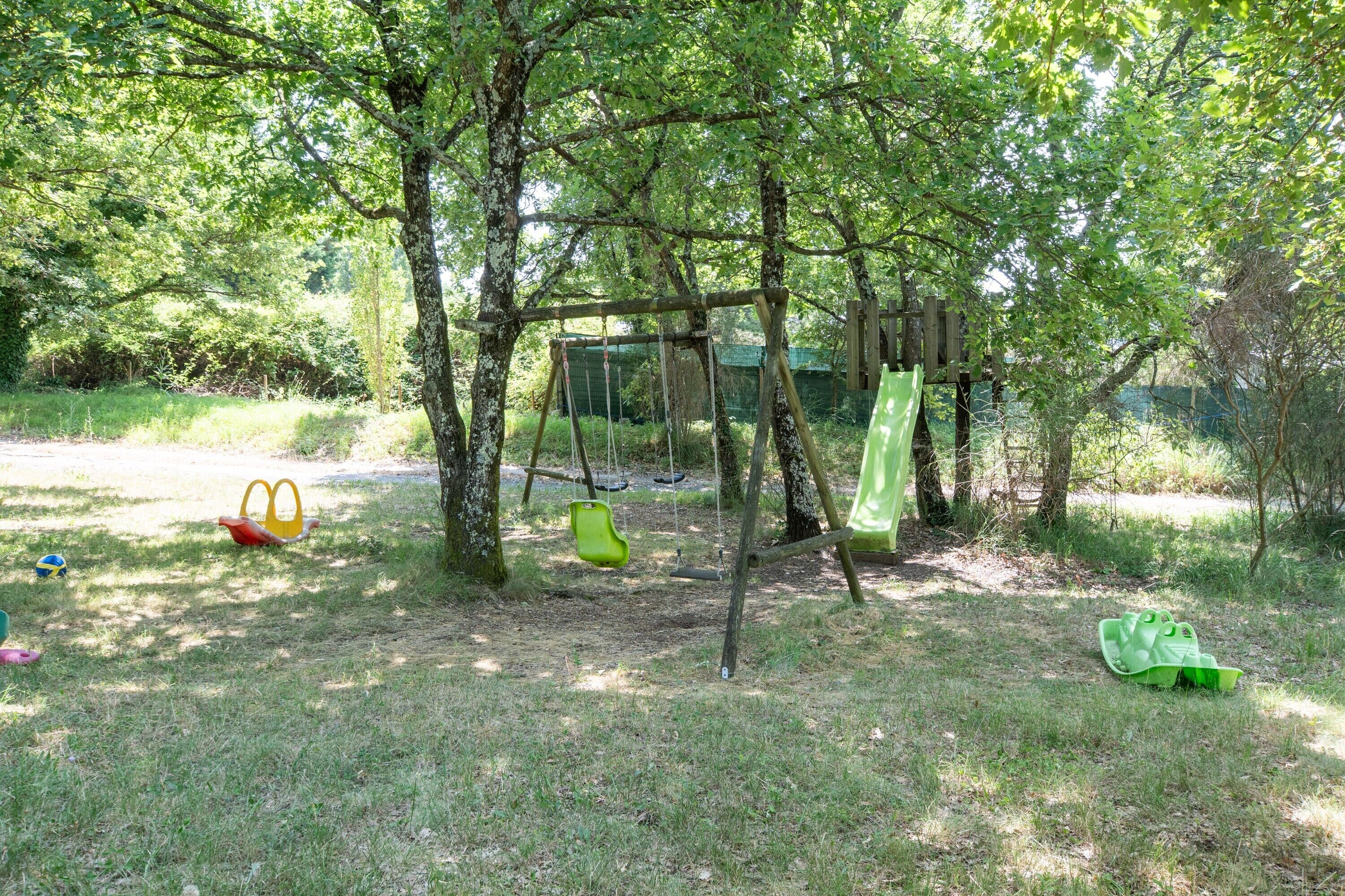A playground with swings and slides, surrounded by trees.