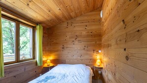 Una habitación de cabaña de madera con una cama, dos lámparas de noche y una ventana con cortinas.