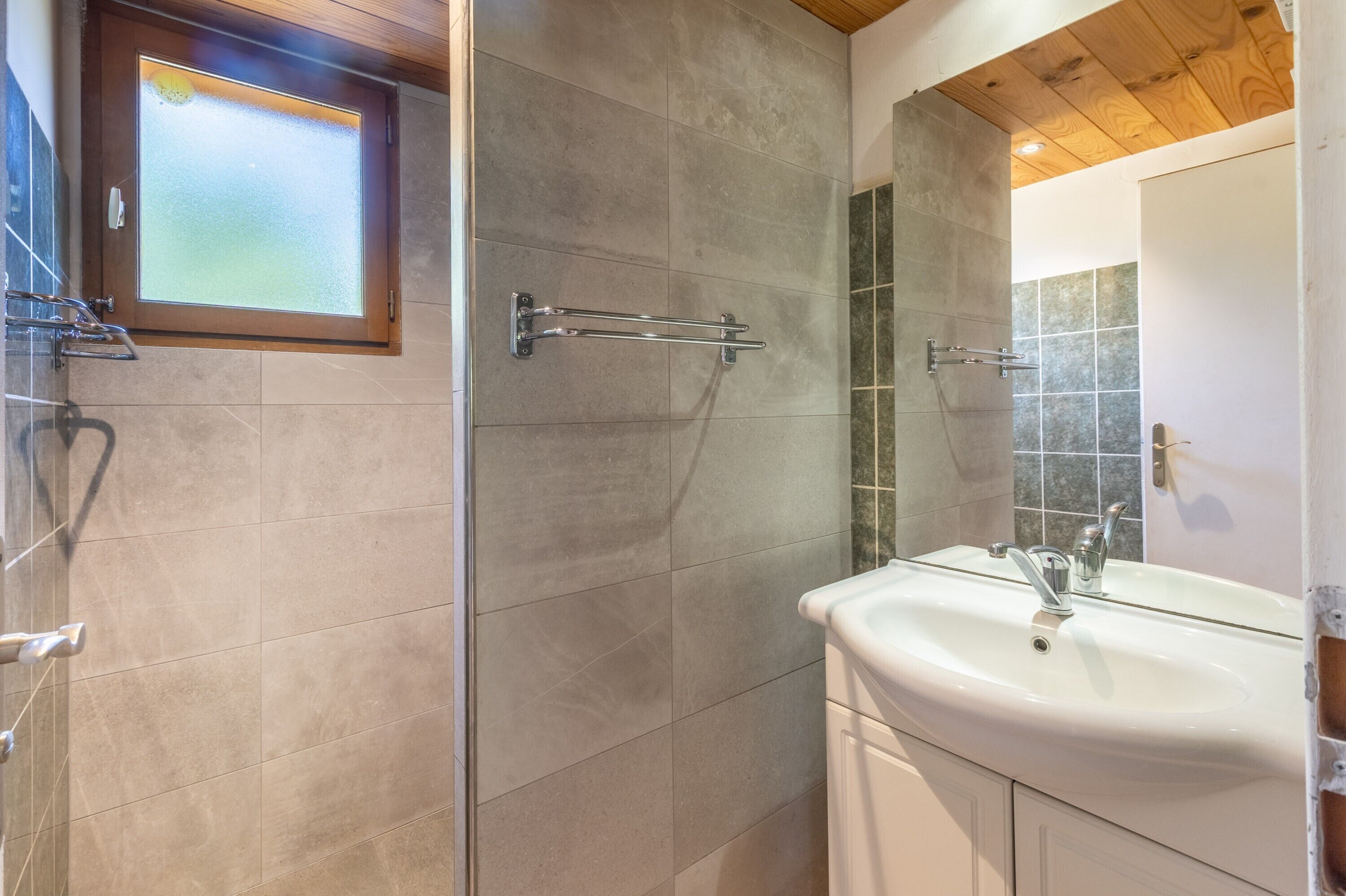 Een badkamer met een douche, een wastafel en een raam.
