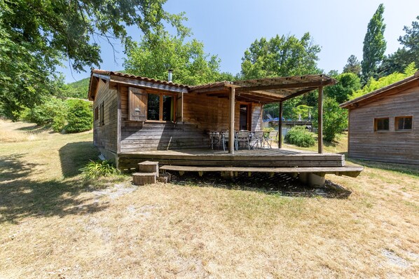 A wooden cabin with a porch, a small deck, and a covered outdoor seating area.