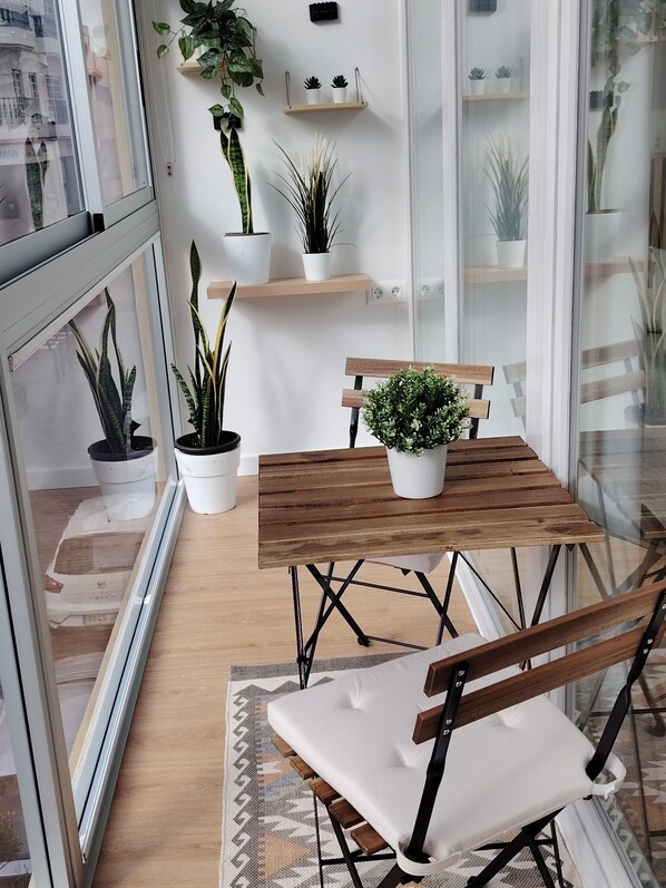Ein Balkon mit Holztisch und Bank, Blumentöpfen und Blick auf GebÀude.