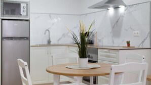 A modern kitchen with white cabinetry, a built-in microwave, and a round wooden table with two white chairs. - 'Suite 1 San Agustin' with Wi-Fi (Icod de los Vinos)