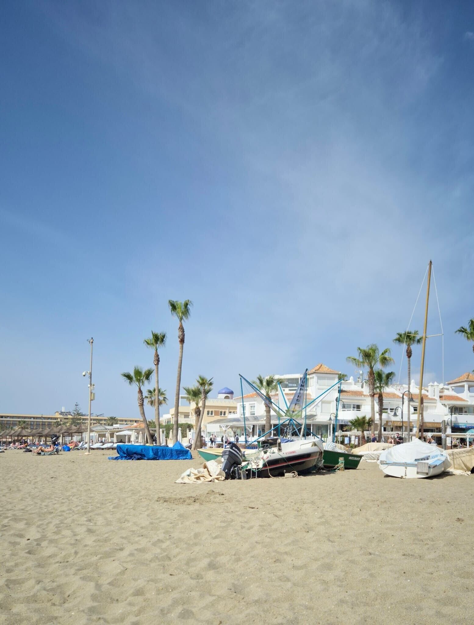 A beach with boats, palm trees, and buildings in the background.