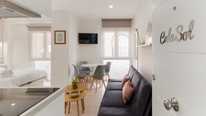 A modern hotel room with a bed, a dining area, a sofa, and a TV.