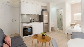 A compact apartment with a kitchenette, a dining area, a living room with a sofa, and a bedroom with a bed and a bedside table.