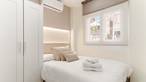 A bedroom with a bed, pillows, a window, and an air conditioning unit.