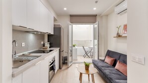 A compact kitchen with modern appliances, a dining area with a small table and chair, and a living space with a sofa and a plant.