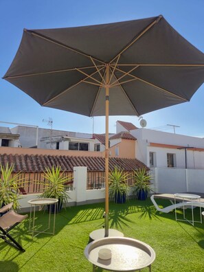 Una terraza en la azotea con una sombrilla grande, mobiliario exterior y plantas en macetas.