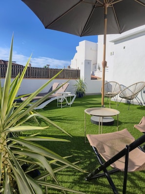 A patio with artificial grass, a round table, two lounge chairs, and a large umbrella.