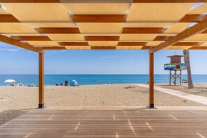 Cubierta de madera junto a la playa con vista al océano y gente disfrutando.