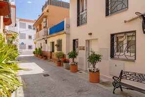 Una calle estrecha con edificios, plantas en macetas y un banco.