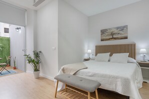 A bedroom with a bed, bedside tables, a bench, a painting, and a door leading to a balcony.