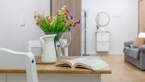 A modern living room with a wooden table, a white chair, a vase with flowers, a wine glass, and an open book. - Vacation Studio 'Estudio San Agustín 45' with Wi-Fi (Icod de los Vinos)