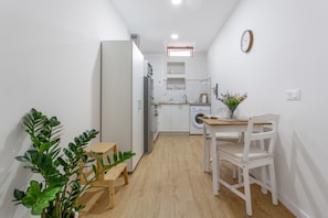 A compact kitchen with a refrigerator, washing machine, and a dining area with a table and chairs.