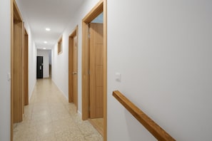 Um corredor com portas de madeira, chão de azulejos e interruptor de luz na parede.