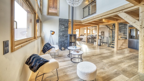 Un salón espacioso con techo alto, vigas de madera, chimenea y comedor, junto a una escalera.