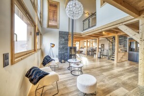Un salón espacioso con techo alto, vigas de madera, chimenea y comedor, junto a una escalera.