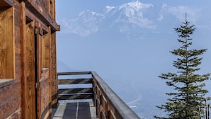 Una cabaña de madera con una escalera que lleva a un balcón con vistas a montañas nevadas.