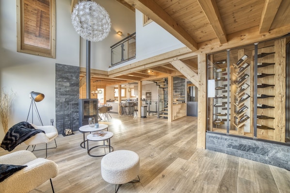 Un vaste espace de vie doté d’un plancher en bois, d’une cheminée, d’un meuble à vin et d’un plafond haut avec des poutres apparentes.