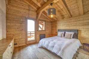 Une chambre aménagée dans une cabane en bois, avec un lit, un luminaire suspendu et une porte donnant sur une terrasse extérieure.