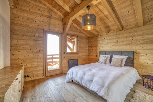 Un dormitorio de cabaña de madera con una cama, una lámpara colgante y una puerta que da a una terraza exterior.