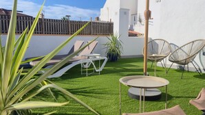 A patio with artificial grass, a round table, two lounge chairs, and a large umbrella. - La Cala Home - Cala Luna – Bright Upper-Floor Studio Steps from the Beach (La Cala de Mijas)