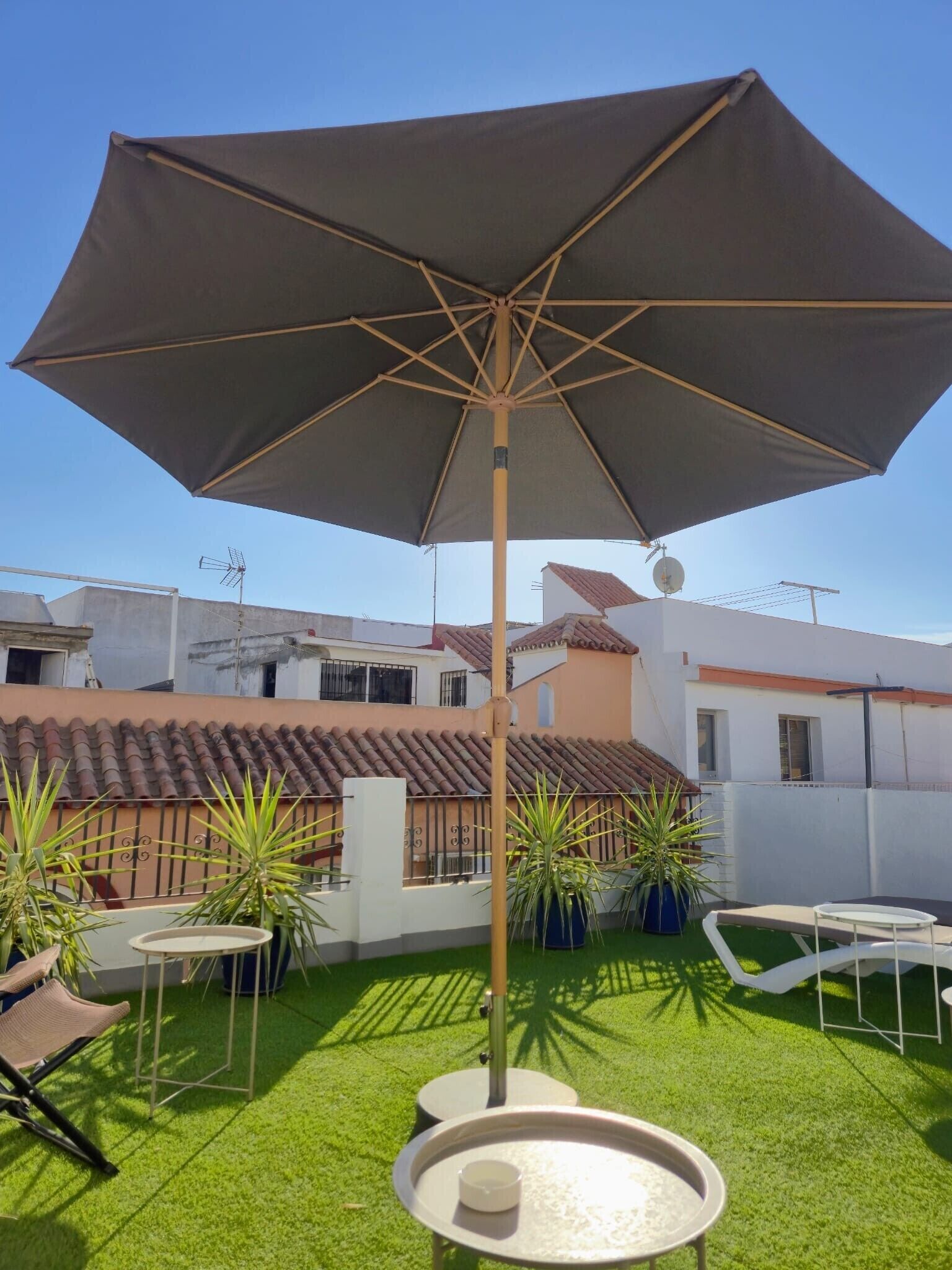 Een terras op het dak met een grote parasol, tuinmeubels en potplanten.