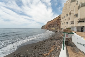 Un hôtel situé sur la côte, avec une plage rocheuse, une falaise et un ciel dégagé.