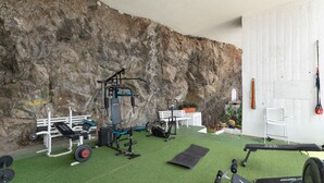 A gym with exercise equipment, a bench, and a wall with a rock-like texture.