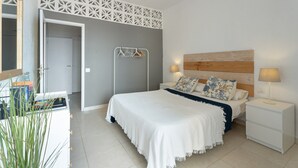 A bedroom with a bed, bedside tables, a wall-mounted light, and a door leading to another room.