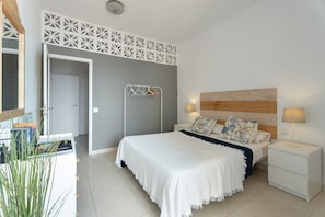 Une chambre à coucher comprenant un lit, des tables de chevet, une lampe fixée au mur et une porte donnant sur une autre pièce.